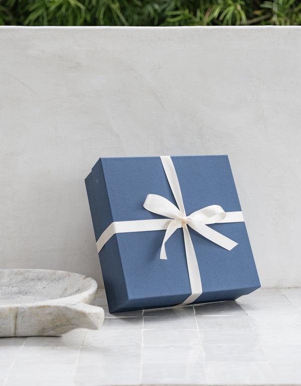Navy Gift Box tied with white ribbon leaning against wall